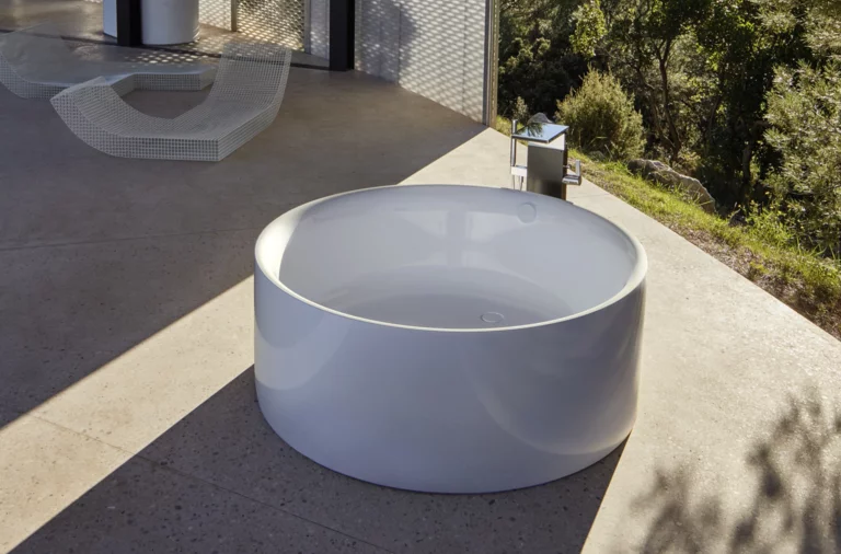 Ronde vrijstaande badkuip van staal-email op terras, modern design, omgeven door natuur en minimalistische omgeving.