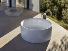 Ronde vrijstaande badkuip van staal-email op terras, modern design, omgeven door natuur en minimalistische omgeving.