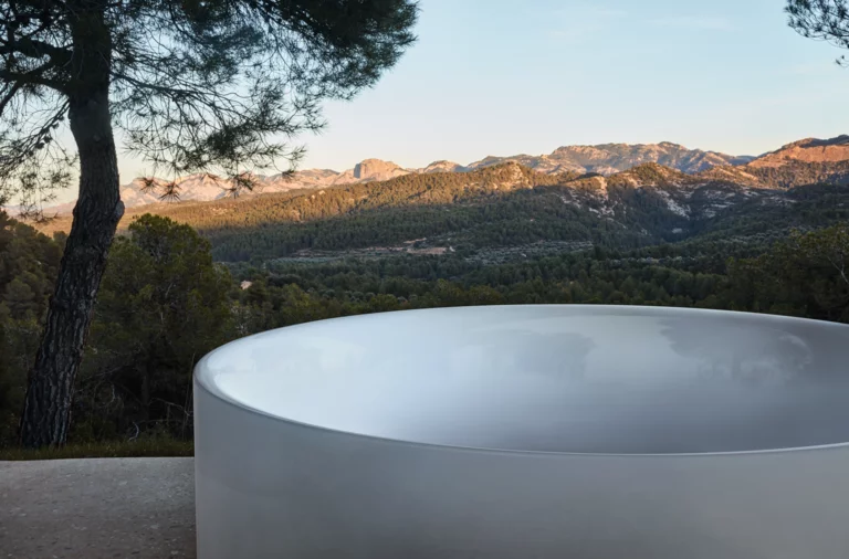 户外景观前，圆形独立搪瓷钢浴缸，光亮，背景有山和树
