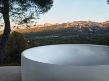 户外景观前，圆形独立搪瓷钢浴缸，光亮，背景有山和树