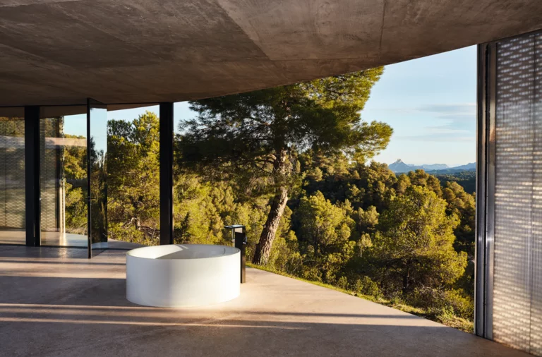 圆形独立搪瓷钢浴缸置于开放空间，大窗前可观森林景色。