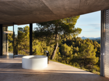 圆形独立搪瓷钢浴缸置于开放空间，大窗前可观森林景色。