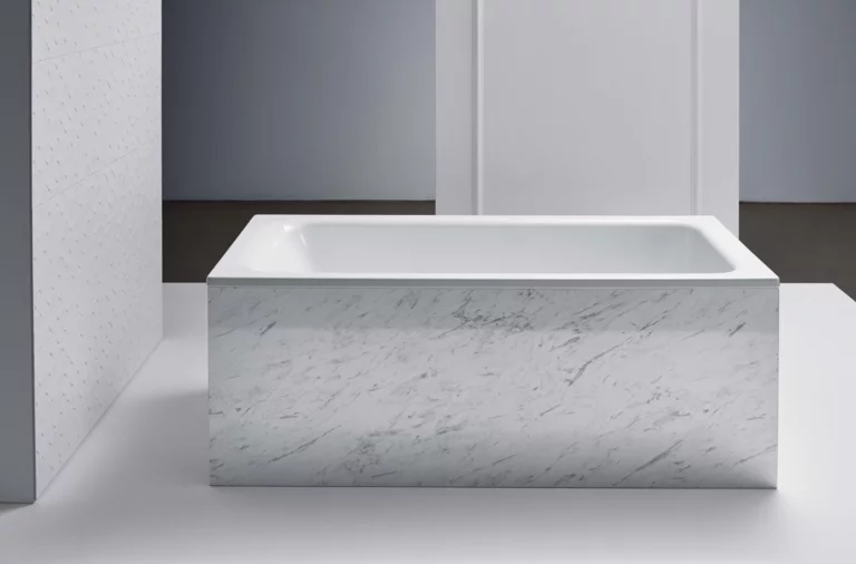 Rechthoekig bad van staal-email met witte, gemarmerde ombouw in moderne badkamer.