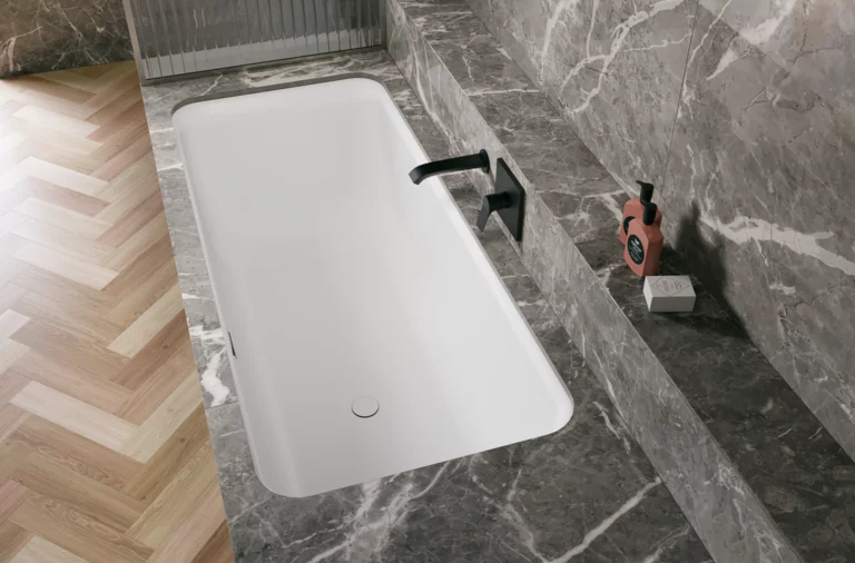 Weiße Badewanne in grauer Nische mit schwarzer Armatur und hellem Fischgrätboden.