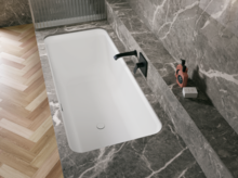 Weiße Badewanne in grauer Nische mit schwarzer Armatur und hellem Fischgrätboden.