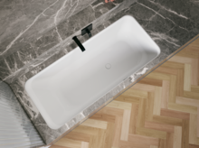 Weiße Badewanne in grauer Nische, schräg von oben gesehen, mit schwarzer Armatur und hellem Fischgrätboden.