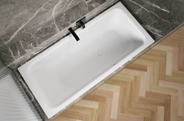 Weiße Badewanne in grauer Nische, schräg von oben gesehen, mit schwarzer Armatur und hellem Fischgrätboden.