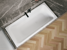 Weiße Badewanne in grauer Nische, schräg von oben gesehen, mit schwarzer Armatur und hellem Fischgrätboden.