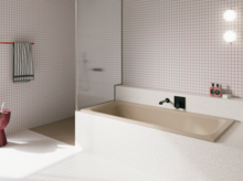 Beigefarbene Badewanne in weiß gefliestem Bad mit Duschbereich, Wandarmatur und rosa Hocker.