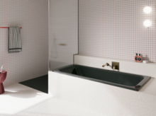 Dunkle Badewanne in weiß gefliestem Bad mit Duschbereich, Wandarmatur und rosa Hocker.