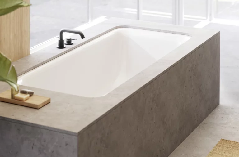 Vasca da bagno incassata rettangolare con rivestimento grigio, rubinetto nero e luce naturale da destra.