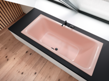 Rechteckige, eingebaute Badewanne in zartem Rosé, mit schwarzer Armatur, vor Fenster und auf hellem Holzboden.