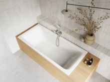 Weiße Badewanne in heller Holzoptik-Einfassung mit Handbrause, Ablage und Vase im gefliesten Bad.