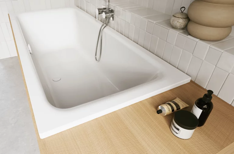 Weiße Badewanne mit heller Ablage, Handbrause und Pflegeflaschen im hell gefliesten Bad.