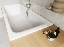 Weiße Badewanne mit heller Ablage, Handbrause und Pflegeflaschen im hell gefliesten Bad.