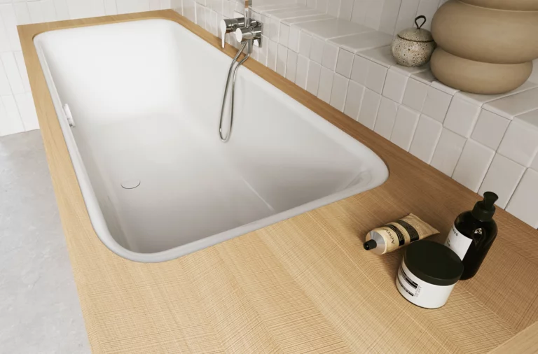 Weiße Badewanne in heller Holzoptik-Einfassung mit Handbrause und Pflegeflaschen im gefliesten Bad.