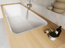 Weiße Badewanne in heller Holzoptik-Einfassung mit Handbrause und Pflegeflaschen im gefliesten Bad.