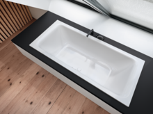 Rechteckige Badewanne aus Stahl-Email, eingebaut in schwarze Fläche, mit Armatur, modernes Design, große Fensterfront.