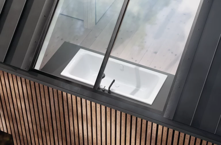 Rechteckige Badewanne aus Stahl-Email unter schrägem Fenster, eingebaut in eine Holzverkleidung.