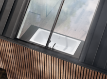 Rechteckige Badewanne aus Stahl-Email unter schrägem Fenster, eingebaut in eine Holzverkleidung.