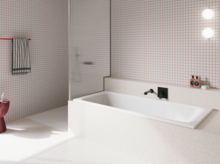 Weiße Badewanne in hell gefliestem Bad mit Duschbereich, Wandarmatur und rosa Hocker.