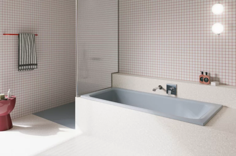 Hellgraue Badewanne in hell gefliestem Bad mit Duschbereich, Wandarmatur und rosa Hocker.
