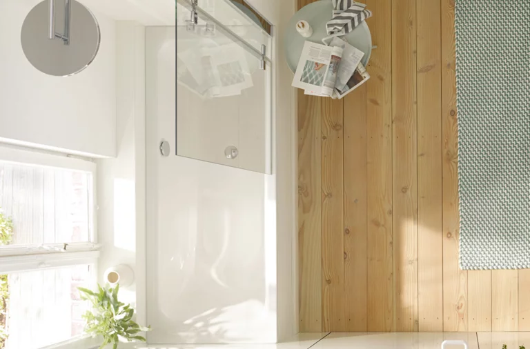 Rectangular steel-enamel bathtub with glass partition in modern bathroom with wood and tile flooring.