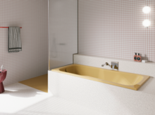 Gelbe Badewanne in hell gefliestem Bad mit Duschbereich, Wandarmatur und rosa Hocker.