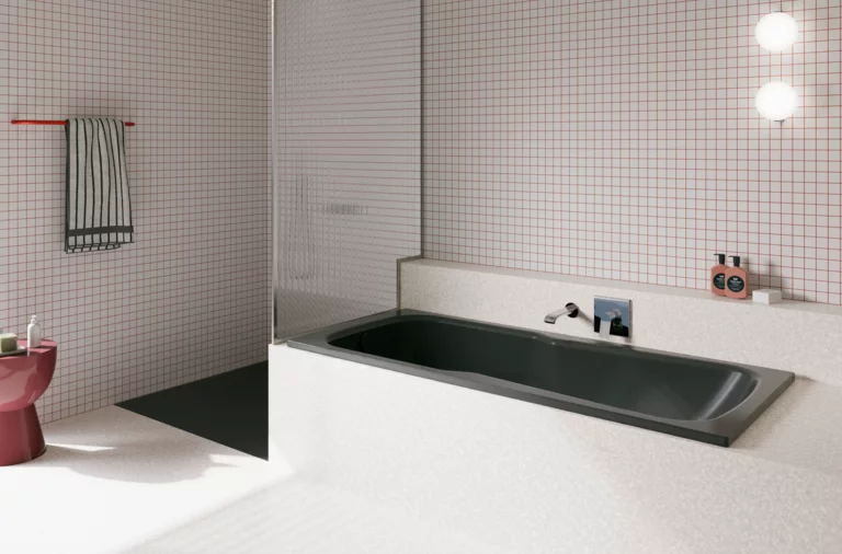 Dunkle Badewanne in hell gefliestem Bad mit Duschbereich, Wandarmatur und rosa Hocker.