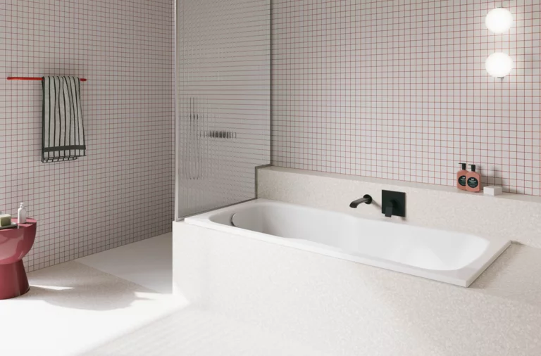 Weiße Badewanne in hell gefliestem Bad mit Duschbereich, Wandarmatur und rosa Hocker.