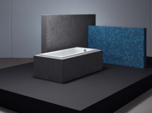 Baignoire rectangulaire en acier émaillé aux bords droits, au design moderne, posée sur une plateforme noire devant des panneaux muraux.