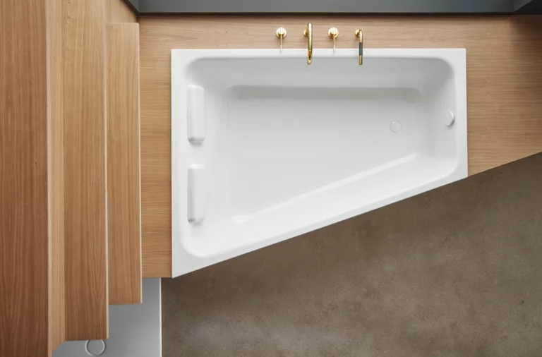Rectangular steel enamel bathtub with sloped side, set in wooden panel, gold fittings, modern look.