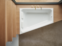 Rectangular steel enamel bathtub with sloped side, set in wooden panel, gold fittings, modern look.