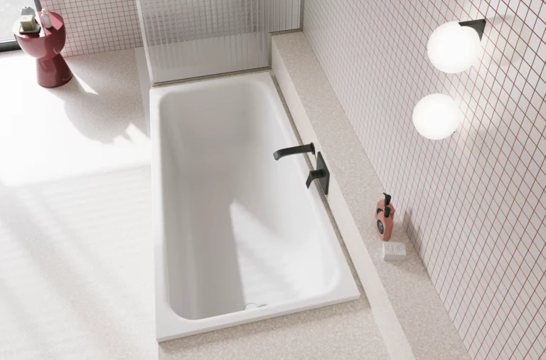 Wit bad in lichte badkamer met witte tegels, donkere kraan, ronde lampen en een rood bijzettafeltje.