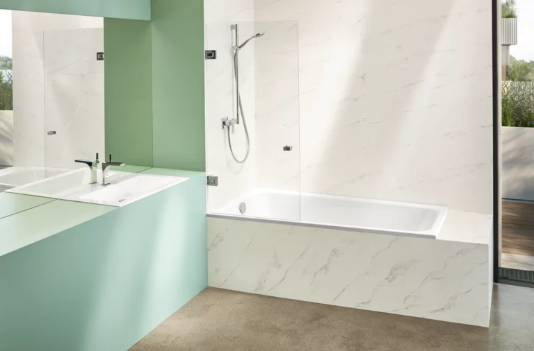 Modernes Bad mit rechteckiger Stahl-Email-Badewanne, Waschbecken auf Einbauplatte, ebenerdigem Boden und heller Wandverkleidung.