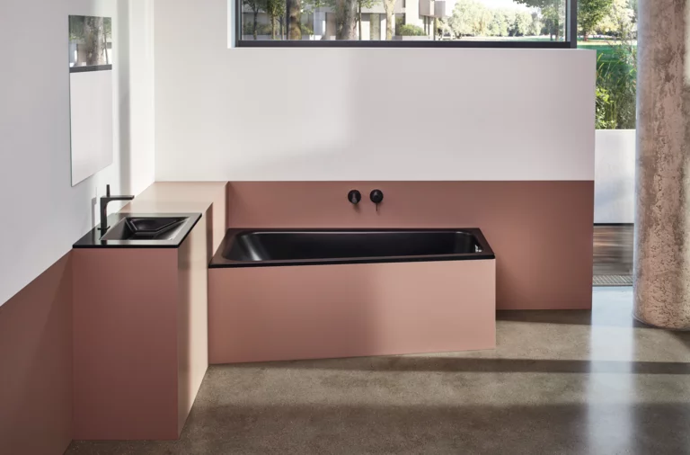 Vasca da bagno rettangolare in acciaio smaltato nera e lavabo su piano d’appoggio in moderno bagno accessibile con finestra.