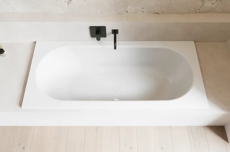 Weiße Badewanne in hellem Bad mit schwarzer Armatur, heller Wandverkleidung und hellem Holzboden.