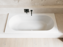 Weiße Badewanne in hellem Bad mit schwarzer Armatur, heller Wandverkleidung und hellem Holzboden.