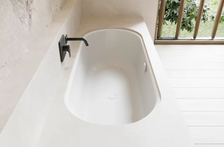 Weiße Badewanne in hellem Bad mit schwarzer Armatur, hellem Boden und Fenster mit Blick ins Grüne.