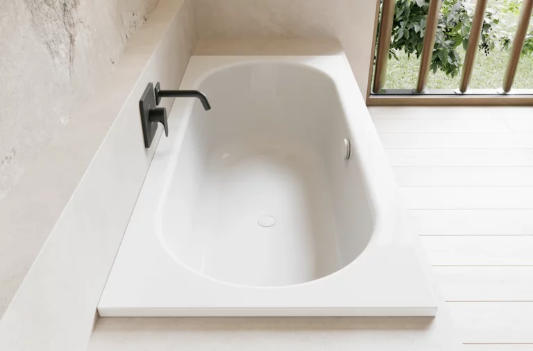 Weiße Badewanne in hellem Bad mit schwarzer Armatur, hellem Boden und Fenster mit Blick ins Grüne.