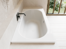 Weiße Badewanne in hellem Bad mit schwarzer Armatur, hellem Boden und Fenster mit Blick ins Grüne.