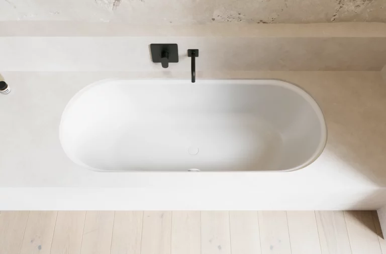 Weiße Badewanne in hellem Bad mit schwarzer Armatur, heller Wandverkleidung und hellem Holzboden.