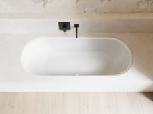 Weiße Badewanne in hellem Bad mit schwarzer Armatur, heller Wandverkleidung und hellem Holzboden.