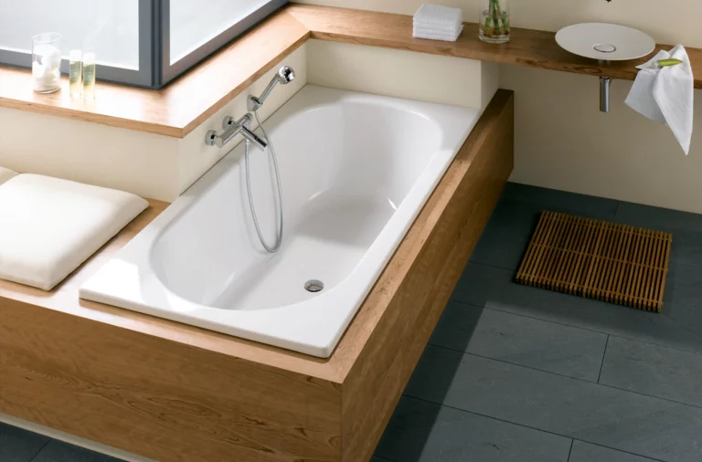 Rectangular steel-enamel bathtub, white surface, built into wood paneling, next to round washbasin on countertop.