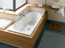 Rectangular steel-enamel bathtub, white surface, built into wood paneling, next to round washbasin on countertop.