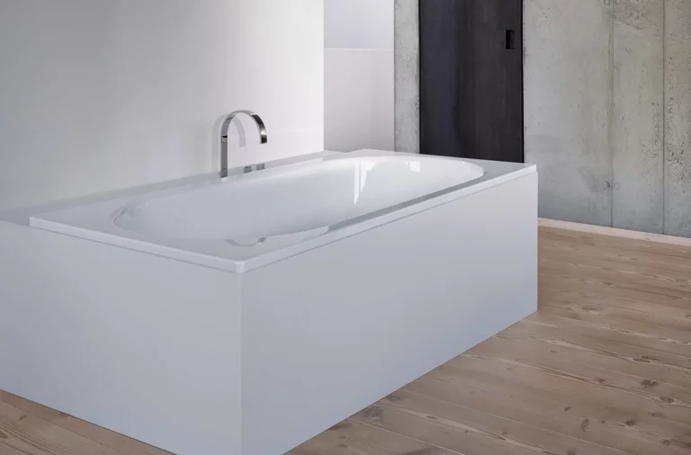 Rectangular steel enamel bathtub with rounded inner edges, installed in modern bathroom with wooden floor.