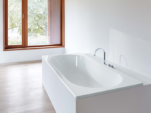 Rectangular steel enamel bathtub in bright setting, built-in with modern fittings and large window in background.