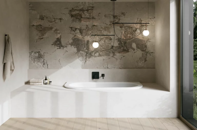 Wit bad in lichte badkamer met witte ombouw, gestructureerde wand, hanglampen en groot raam.