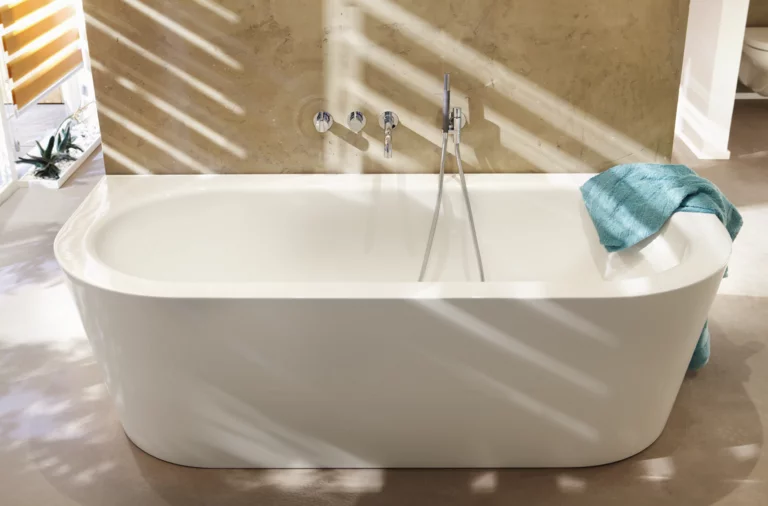 Bañera ovalada independiente de acero esmaltado junto a la pared, toalla en el borde, grifería moderna.