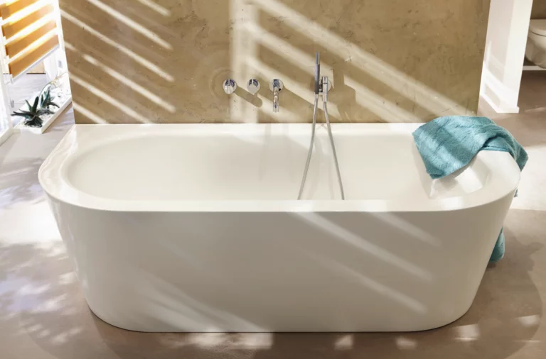 Freistehende, ovale Badewanne aus Stahl-Email vor Wand, Handtuch am Rand, moderne Armaturen.